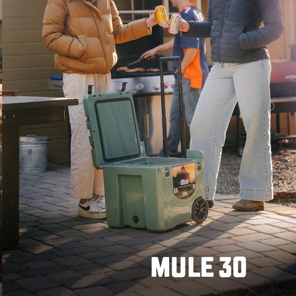 People standing around a Green Mule 30 QT Wheeled Cooler on their back patio